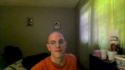 Bald man with glasses sits thoughtfully in a softly lit room - yesvids.com