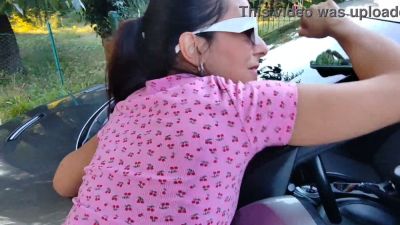Young woman in pink dress gives bold outdoor blowjob beside a car while someone watches - yesvids.com