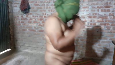 Nude figure in a brick room adjusts green headcloth under dim light - yesvids.com